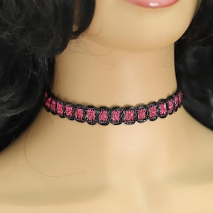 May include: A black choker necklace with a pink and black braided design.