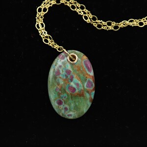May include: A gold chain necklace with a green and pink oval pendant. The pendant has a mottled pattern of green, pink, and brown.