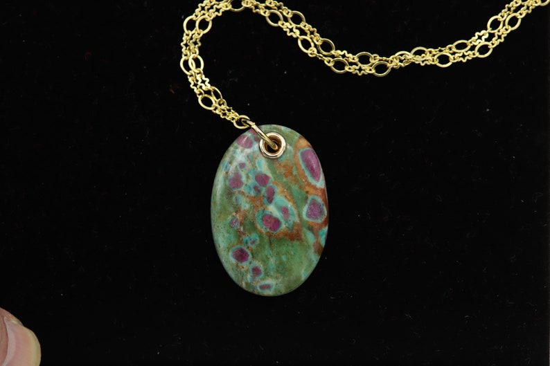 May include: A gold chain necklace with a green and pink oval pendant. The pendant has a mottled pattern of green, pink, and brown.