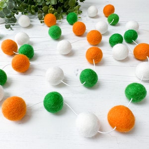 May include: A garland of felt balls in white, orange and green. The balls are strung together with white thread.