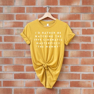 May include: A mustard yellow t-shirt with the text "I'd rather be watching the 1999 cinematic masterpiece "The Mummy""