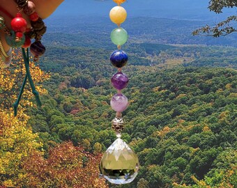 Puede incluir: Un atrapasoles de cristal de chakra con un cristal facetado transparente y siete cuentas de piedras preciosas de colores. Las cuentas son rojas, naranjas, amarillas, verdes, azules, moradas y rosas. El atrapasoles cuelga de un cordón blanco.