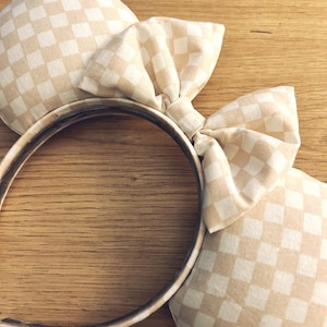 May include: A pair of beige and white checkered mouse ears with a large bow. The headband is brown.