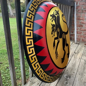 May include: A round, black and red shield with a gold trim and a gold silhouette of a three-headed dog on the front.