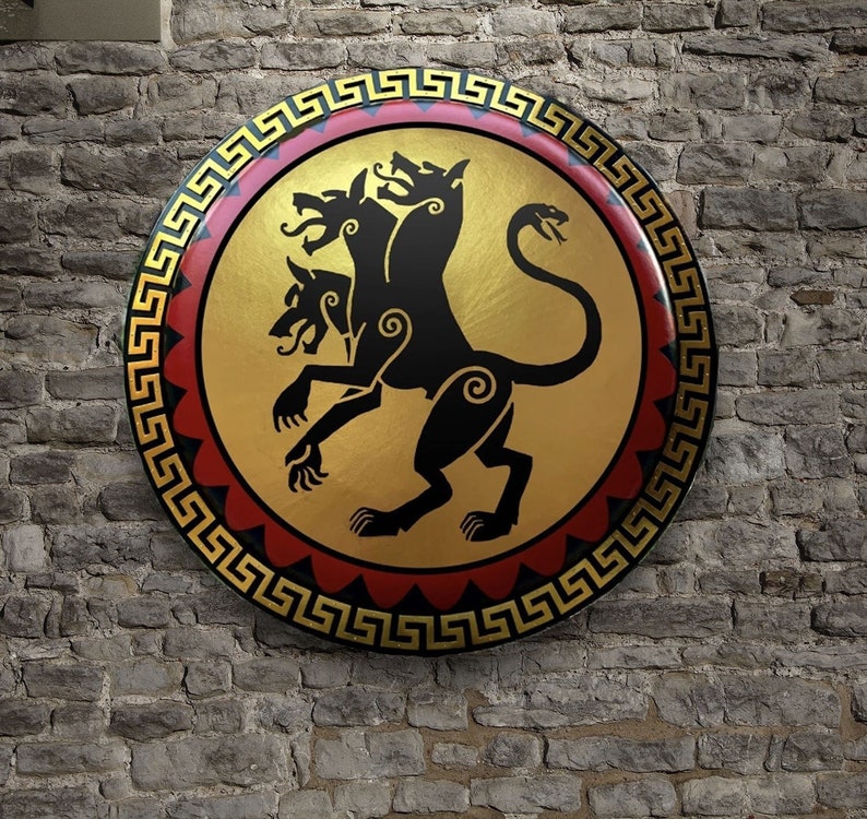 May include: A gold shield with a black three-headed dog design. The shield has a red and gold border with a Greek key pattern.