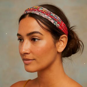 May include: A multi-strand braided headband featuring a vibrant mix of red, pink, and floral patterned fabric strips. The accessory is constructed from several intertwined fabric cords, creating a textured, layered appearance across the top of the head.