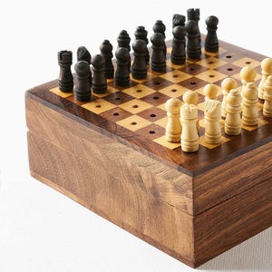 May include: A wooden chess set featuring a square board with a dark and light brown checkered pattern. The board includes small holes for securing the individual chess pieces. The set includes dark brown and light beige wooden chess pieces.