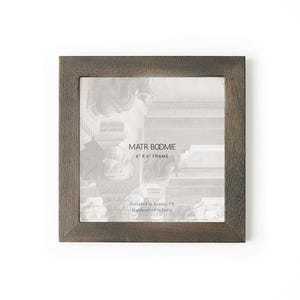 May include: A square dark brown wooden picture frame with a visible wood grain texture. The insert features the text MATR BOOMIE, 6" X 6" FRAME, Designed in Austin, TX, and Handcrafted in India over a faint grayscale architectural image.