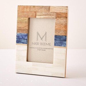 May include: A rectangular picture frame featuring a multi-material border. The top section is made of light brown wood, the middle has horizontal blue strips, and the bottom is composed of white rectangular pieces. The insert reads MATR BOOMIE.