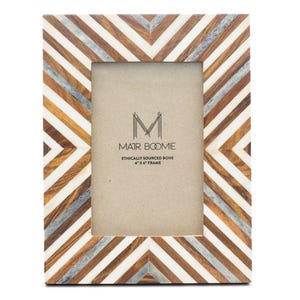 Puede incluir: Un marco de fotos rectangular con un patrón de chevrón hecho de tiras alternas de madera marrón, hueso blanco y resina gris. El inserto central muestra el texto MATR BOOMIE ETHICALLY SOURCED BONE 10 cm X 15 cm FRAME. El marco tiene orientación vertical.