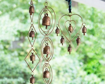 May include: Three hanging wind chimes made of weathered copper-toned metal. One features diamond-shaped frames, another has concentric oval rings, and the third is heart-shaped. Each frame holds small, rustic bells suspended by metal loops.
