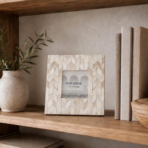 Puede incluir: Un marco de fotos cuadrado con un patrón de espiga en color crema y beige hecho de azulejos incrustados. La inserción central muestra el texto MATR BOOMIE 3" X 3" FRAME. El marco tiene una superficie plana y lisa con una abertura cuadrada.