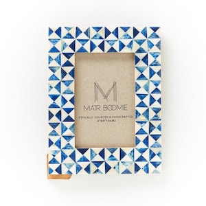 May include: A rectangular photo frame with a geometric pattern of blue and white triangles. The frame is labeled "4"x6" Frame" and features the text "MAIR BOOMIE" and "ETHICALLY SOURCED & HANDCRAFTED". The frame has a neutral-colored backing.