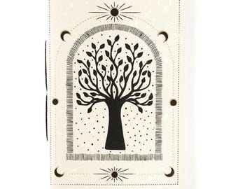 May include: A rectangular notebook with a cream-colored cover featuring a black ink illustration of a tree centered within an arched frame. The design includes sun and moon motifs at the top and bottom, with small black dots scattered throughout.