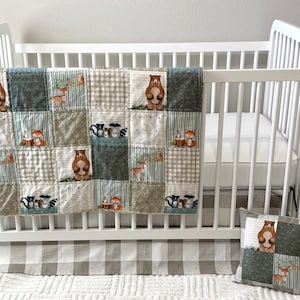 May include: A white crib with a woodland-themed quilt and matching pillow. The quilt features squares with forest animals like bears, deer, and foxes. The crib skirt has a gray and white checkered pattern. The pillow has a bear and deer design.