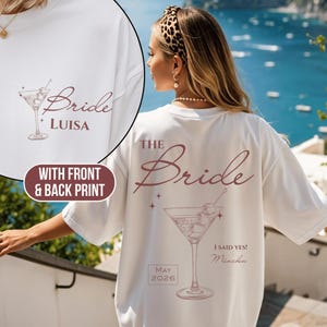 Könnte beinhalten: Weißes T-Shirt mit Front- und Backprint. Auf der Vorderseite steht das Wort "Bride" und der Name "LUISA" mit einer Cocktail-Illustration. Auf der Rückseite steht "THE Bride", eine Cocktail-Illustration und "I SAID YES! München, MAY 2026".