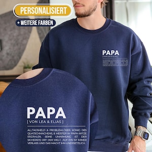 Op de afbeelding: Marineblauw sweatshirt met het woord "PAPA" in het wit gedrukt. Het sweatshirt heeft extra tekst onder het woord "PAPA". De bovenkant van het sweatshirt heeft de tekst "PERSONALISIERT" en "+ WEITERE FARBEN".