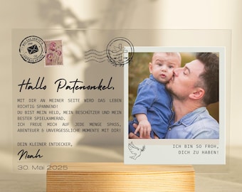 Puede incluir: Un expositor de fotos de acrílico transparente con una base de madera. La pantalla presenta una fotografía de un hombre besando a un bebé, acompañada de texto en alemán. El texto incluye la fecha 30 de mayo de 2025 y las palabras "Hallo Patenonkel."
