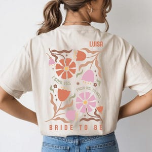 May include: Beige t-shirt with a floral design in orange, pink, and brown. The text includes "I said yes", "From Ms. to Mrs.", "Bride to be", and the name "Luisa".