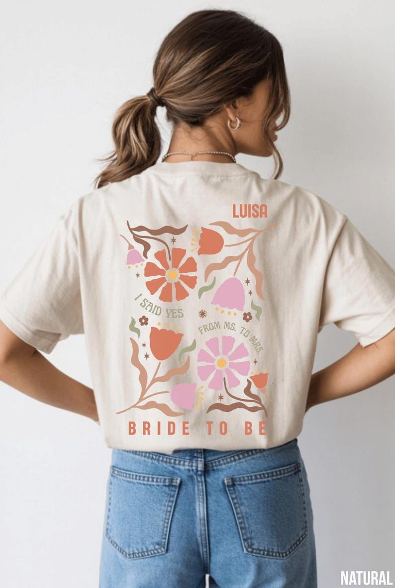May include: Beige t-shirt with a floral design in orange, pink, and brown. The text includes "I said yes", "From Ms. to Mrs.", "Bride to be", and the name "Luisa".
