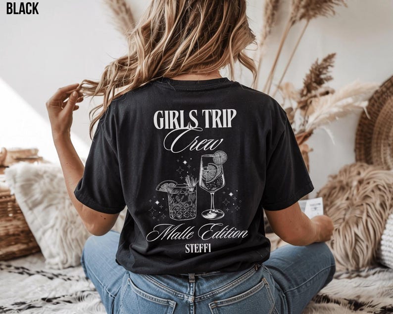 Puede incluir: Camiseta negra con el texto blanco "GIRLS TRIP Crew Malle Edition STEFFI". El dise&ntilde;o incluye ilustraciones de dos c&oacute;cteles con adornos c&iacute;tricos. La camiseta es de estilo casual, adecuada para una salida en grupo.