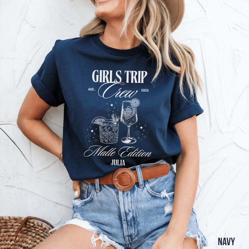 Puede incluir: Camiseta azul marino con el texto "GIRLS TRIP Crew" y "Malle Edition JULIA" en escritura blanca. La camiseta presenta ilustraciones de dos c&oacute;cteles. Se combina con pantalones cortos de mezclilla y un cintur&oacute;n marr&oacute;n.