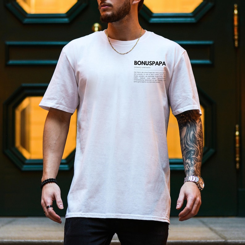 May include: White t-shirt with the text "BONUSPAPA" and a definition of the word. The definition is in black text on a white background.