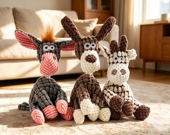 May include: Three plush animal toys: a donkey, a dog, and a giraffe. The donkey is gray with pink ears and muzzle, the dog is brown and white, and the giraffe is white with brown spots. All have googly eyes and are sitting on a rug.