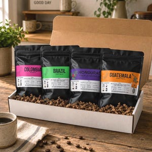 May include: A cardboard gift box containing four black coffee bags labeled Colombia, Brazil, Honduras, and Guatemala. Each bag features a distinct colored label: pink, green, purple, and orange. The box is filled with brown paper filler.