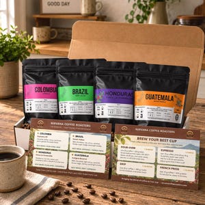 May include: A cardboard box containing four black coffee bags labeled Colombia, Brazil, Honduras, and Guatemala, accompanied by two informational cards from Nirvana Coffee Roasters detailing brewing ratios and flavor profiles for each coffee origin.