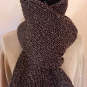 May include: A brown knitted scarf with a textured pattern. The scarf is folded and draped over a mannequin.