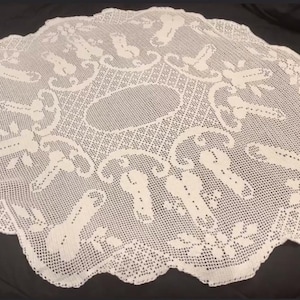 Puede incluir: Doily de crochet blanco con un delicado patrón floral. El doily es circular y tiene un borde festoneado.
