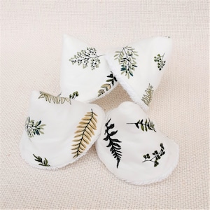 May include: Four white cotton reusable makeup remover pads with a white fuzzy trim. The pads have a green and brown leafy pattern.
