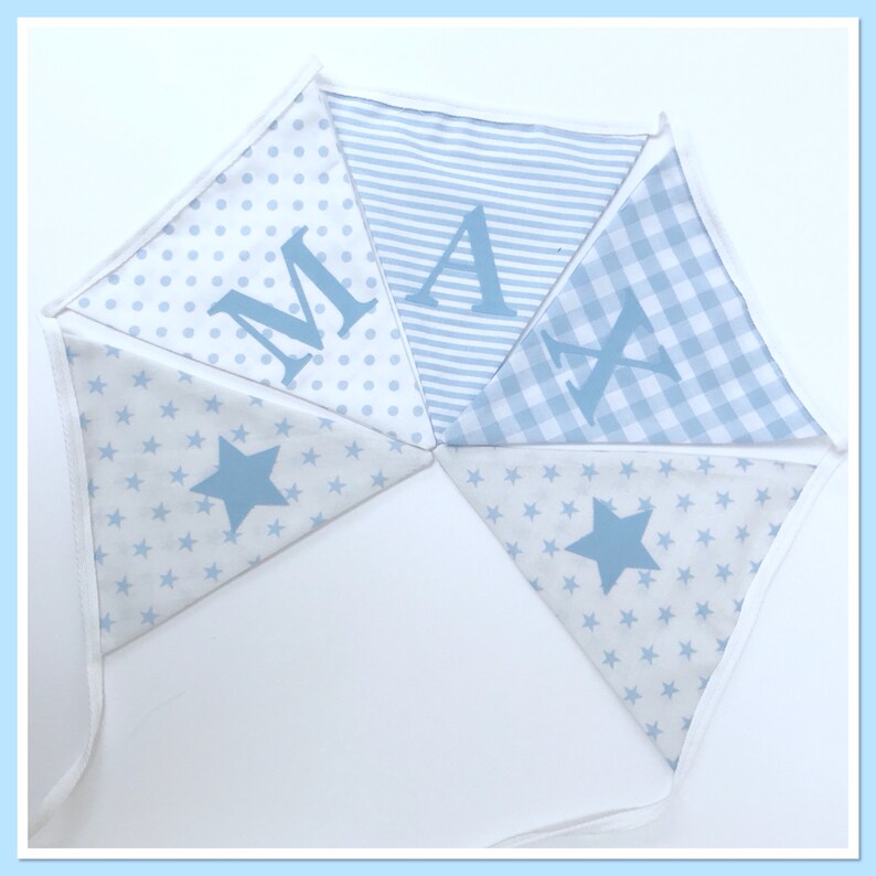 May include: A blue and white bunting with the name "MAX" spelled out in blue letters. The bunting is made of different fabrics with various patterns, including stars, polka dots, stripes, and gingham.