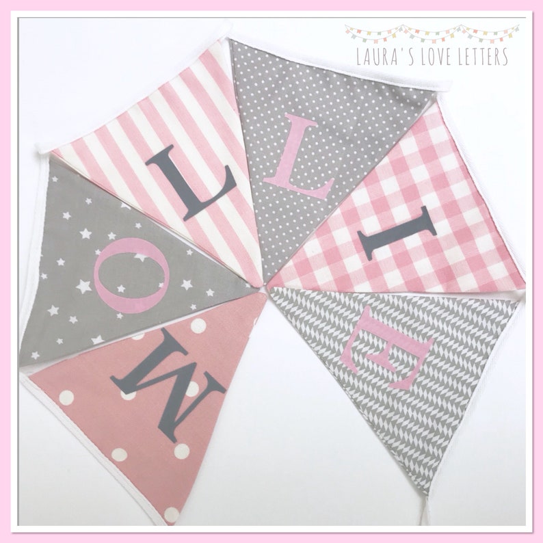 May include: A pink and gray fabric banner with the word "LOVE" spelled out in large, gray letters. The banner is made of different patterned fabrics, including stripes, polka dots, and stars.
