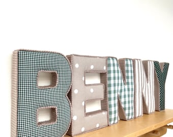 May include: Five plush, three-dimensional fabric letters spelling the name BENNY. The letters feature varied patterns including dark green gingham, beige with white polka dots, light green gingham, and beige vertical stripes, all with ribbed trim.