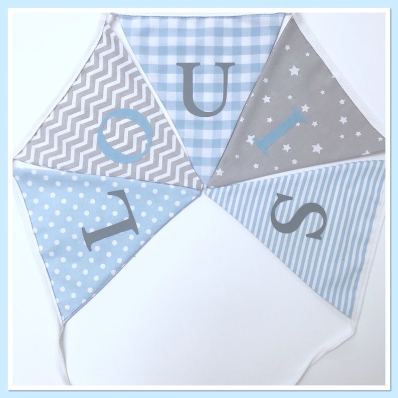May include: A blue and gray fabric banner with the letters "LOUIS" spelled out in gray. The banner is made of different patterns, including polka dots, stripes, gingham, and stars.