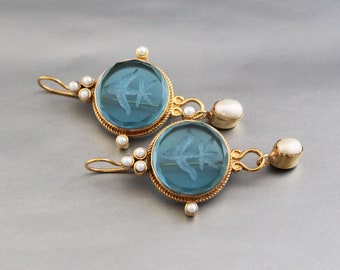 May include: A pair of gold earrings with blue glass cabochons and white pearl accents. Each earring features a delicate etched design of a bird.