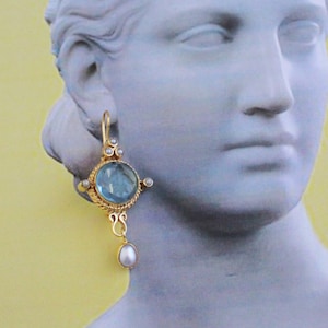 K&ouml;nnte beinhalten: Goldene Ohrh&auml;nger mit einem blauen Edelstein und einem Perlen-Tropfen. Die Ohrringe haben ein zartes, filigranes Design.