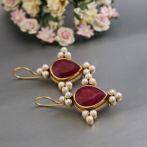 May include: A pair of gold earrings with red gemstone drops and white pearl accents.