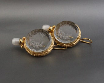 Puede incluir: Un par de pendientes de oro con piedras de cristal transparente que presentan un diseño de hoja tallada. Cada pendiente tiene un pequeño acento de perla blanca.