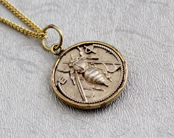 Peut inclure: Un collier en chaîne dorée avec un pendentif rond représentant une abeille argentée. Le pendentif a une surface texturée et un motif d'abeille en relief.