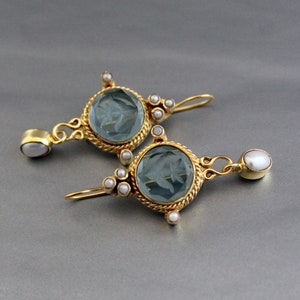 K&ouml;nnte beinhalten: Ein Paar goldene Ohrringe mit blauen Glassteinen und wei&szlig;en Perlenakzenten. Die Ohrringe haben ein detailliertes Design mit einem seilartigen Rand um die Steine.