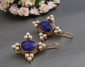 May include: A pair of gold earrings with blue gemstone accents and white pearl embellishments. The earrings have a cross-shaped design with a blue oval gemstone in the center of each cross.