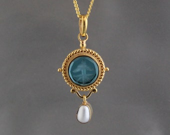 May include: A gold pendant necklace with a blue glass cameo featuring a tree design. The pendant is attached to a pearl drop.