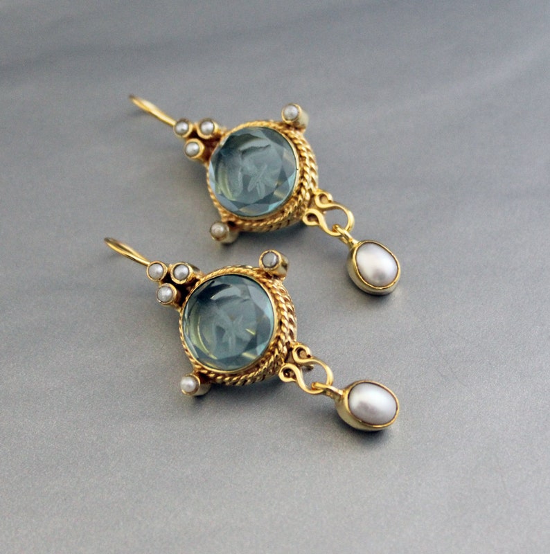 K&ouml;nnte beinhalten: Ein Paar goldene Ohrringe mit blauen Edelstein-Tropfen und Perlen-Akzenten.