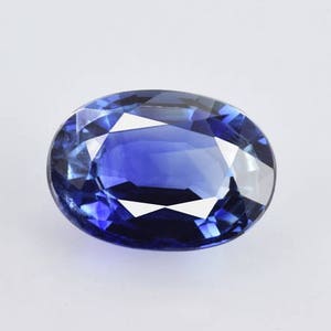 Op de afbeelding: Een diepblauwe ovale saffier edelsteen met een facetgeslepen vorm.