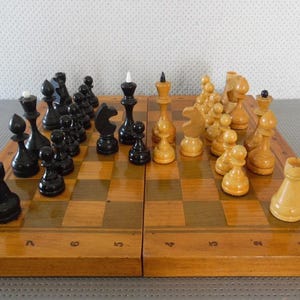 May include: A wooden chessboard with black and white pieces. The board is open and the pieces are set up for a game. The board has numbers 1-8 on each side.
