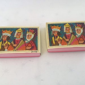 May include: Two rectangular boxes with a pink base and a mosaic-style image of three figures wearing crowns. The figures are depicted in shades of red, orange, and yellow against a teal background. The word "Prestige" is printed on the top of the box.