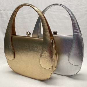 May include: Two vintage handbags, one gold and one silver, with curved handles and a textured finish. The bags have a rounded shape and a clasp closure. The gold bag is on the left, and the silver bag is on the right.